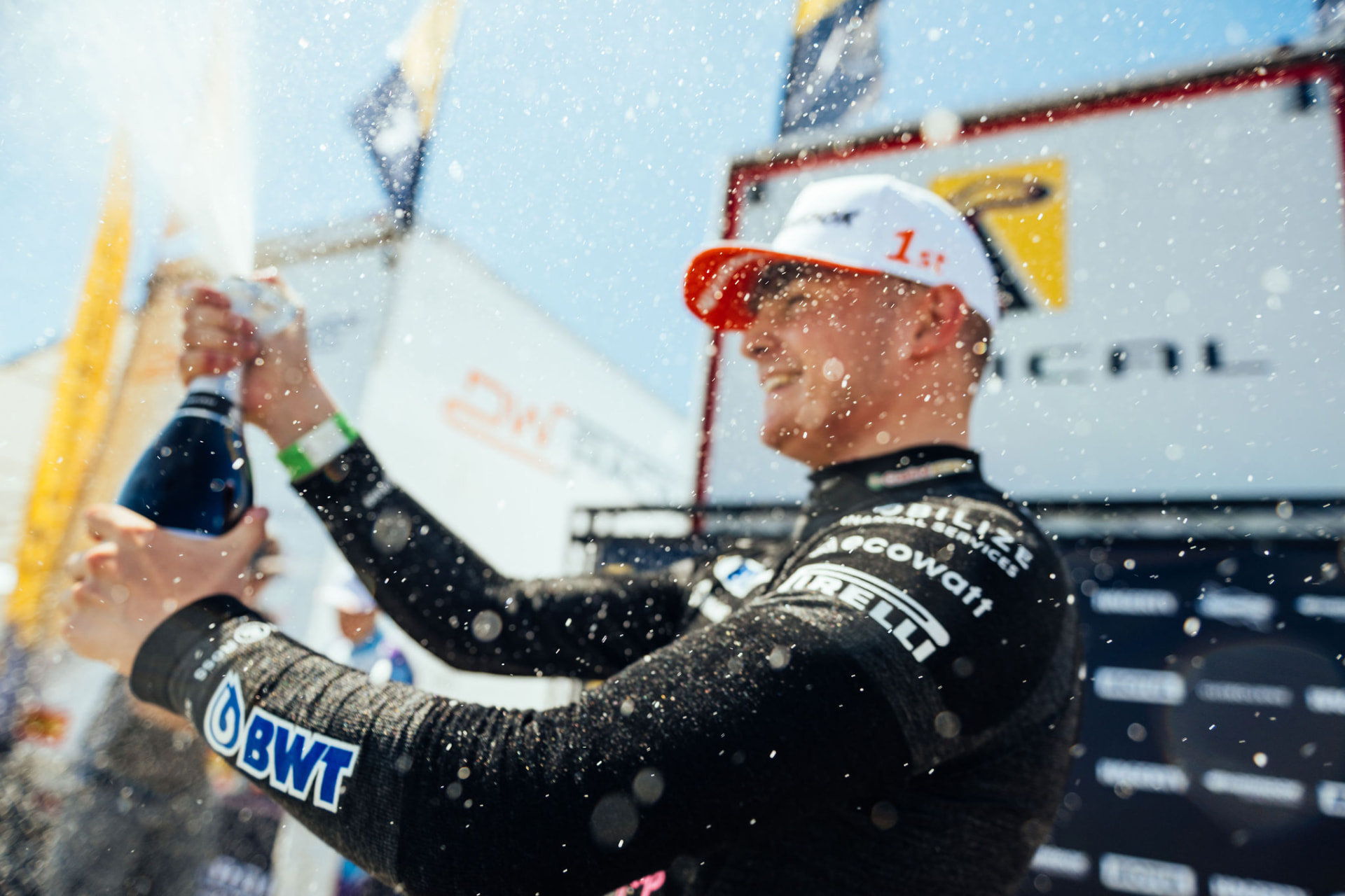 Race driver celebrating a first-place victory on the podium with champagne